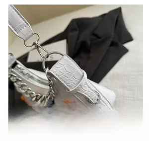 Close-up of silver metal hooks and chain on white crocodile pattern handbag