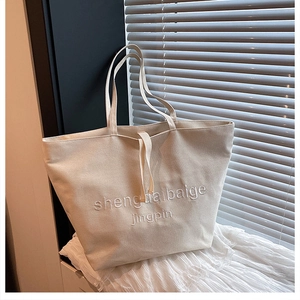 Close-up of minimalist cream white canvas tote bag with embroidered letters on a windowsill