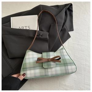 Close-up of green checkered underarm bag with a brown bow on a grey suit background