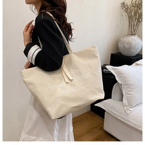 Detail of minimalist beige canvas tote bag with textured lettering and durable straps