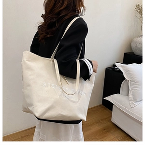Detail of white embroidered text on high-quality off-white canvas tote bag with long straps