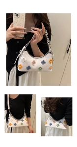 Detail of white crocodile pattern baguette bag with colorful plush floral decorations