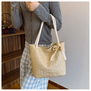 Detail of woven straw tote bag featuring white cotton rope handles and a lace bow accent