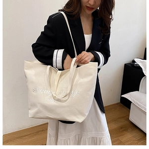 Detail of cream canvas tote bag featuring premium letter embroidery and dual handles