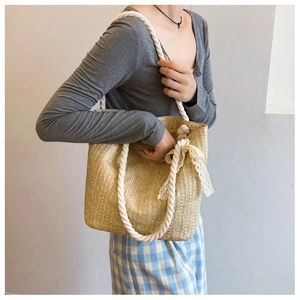 Detail of straw shoulder bag featuring a white lace bow and thick cotton rope handle