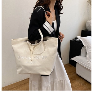 Detailed view of cream canvas tote bag with embroidery on a stylish model