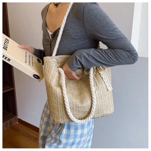 Detail view of woven straw tote bag with white cotton rope handles and lace bow decoration