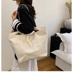 Detailed side view of a large cream canvas tote bag worn by a model in a cozy setting