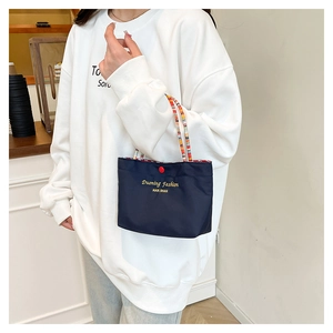 Close-up of navy blue mini tote bag with colorful braided handle and red snap button detail