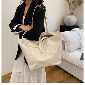 Close-up of a cream canvas tote bag with white embroidery detail on a cozy background