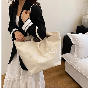Lifestyle view of a large cream canvas tote bag with elegant embroidery on a shoulder strap