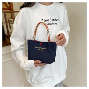 Detail of navy canvas handbag featuring colorful braided handles and gold logo lettering