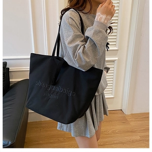 Detail of embossed lettering on a large black canvas tote bag for casual daily use