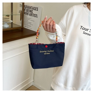 Detail der dunkelblauen Nylon-Handtasche mit buntem Flechtgriff und rotem Knopf