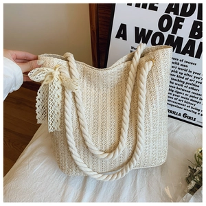 Macro detail of creamy straw tote bag with white rope handles and delicate lace bow
