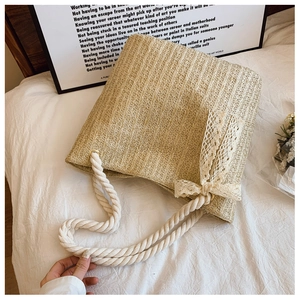 Detail of hand-woven straw tote bag with cotton rope handles and lace bow decoration