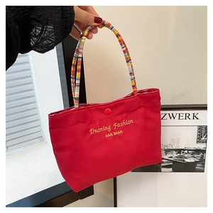 Detail showing the red fabric mini tote bag with colorful braided rope handle and gold text