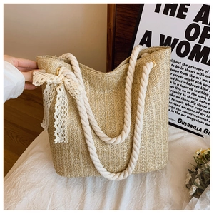 Detailed close-up of straw tote bag featuring thick white rope handles and lace bow decoration