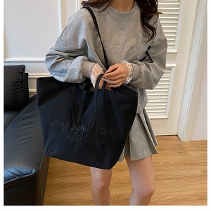 Detail of a large black tote bag with embossed letters worn by a model in a room