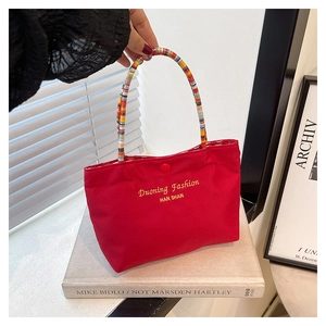 Detail of red canvas phone bag featuring colorful braided handles and yellow embroidery