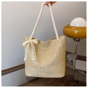 Detail of woven straw tote bag featuring white rope handles and cream lace bow accent