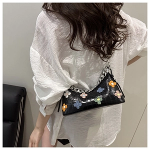 Detail of black crocodile texture shoulder bag with colorful 3D floral accents