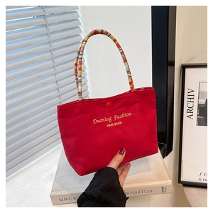 Detail of red canvas tote bag with vibrant braided handles and embroidery