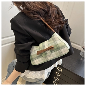 Close-up of green checkered baguette bag with brown leather bow and strap on model
