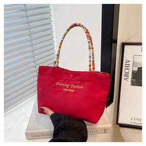 Detail of vibrant red fabric handbag featuring a colorful beaded handle and logo print
