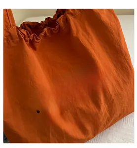 Close-up of orange lightweight nylon tote bag with drawstring detail and logo