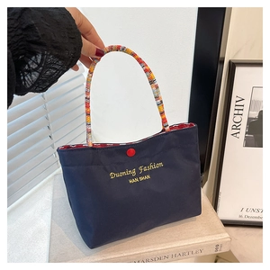 Detail of navy blue canvas phone bag featuring colorful braided handles and red button