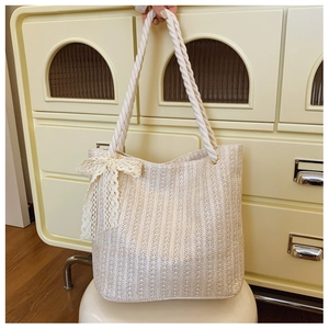 Detail of beige woven straw tote bag featuring creamy lace bow and cotton rope handles