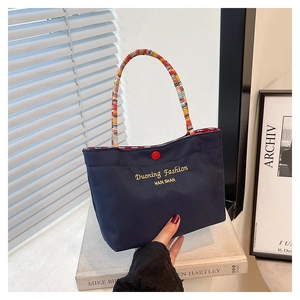 Detail of navy blue mini tote bag featuring colorful braided handles and a red button