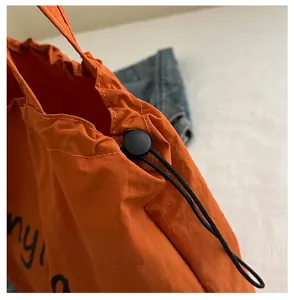 Detail of orange drawstring tote bag showing high-quality nylon fabric and cord stopper