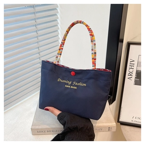 Detailed view of navy blue nylon handbag with colorful woven handle and red button closure
