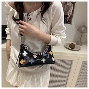 Detail of black faux crocodile leather shoulder bag with colorful floral appliques and silver chain