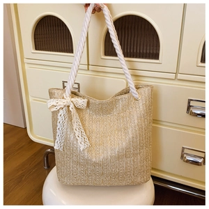 Detail of straw woven tote bag featuring white cotton rope handles and lace bow accent