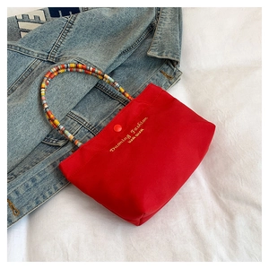 Detail of red canvas tote with colorful beaded handle and gold embroidery accents