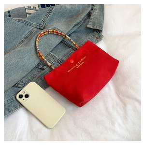 Detail of red canvas mini handbag with colorful beaded handle and snap closure button