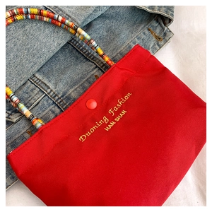 Close-up of bright red canvas phone bag featuring colorful braided handles and gold embroidery