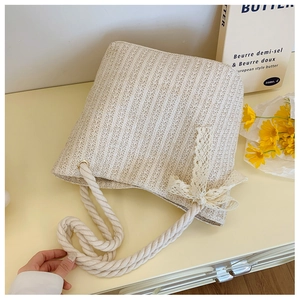 Detail of woven straw bag texture featuring a delicate white lace bow accent and rope handle