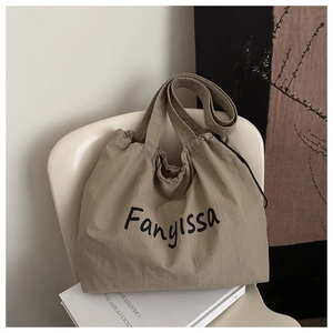 Detail of khaki large capacity tote bag with Fanyissa logo and drawstring closure on chair