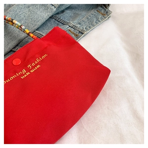 Detail of red fabric phone bag with beaded handle and gold embroidery on denim background