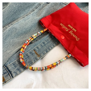 Detail of red canvas phone bag featuring colorful beaded handle and fine embroidery