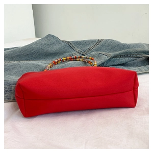 Detail of red canvas tote bag with unique colorful beaded circular handle and casual denim