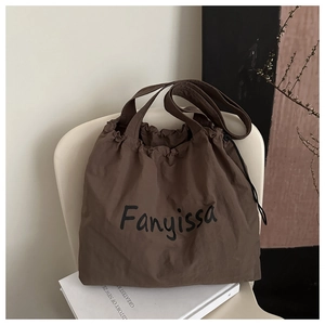Detail of deep coffee nylon drawstring tote bag with letter print on a minimalist chair
