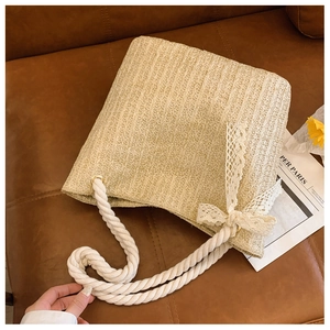 Detail of straw woven tote bag with white lace bow and cotton rope handle on sofa