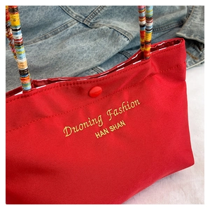 Detail of red canvas tote with yellow embroidery and colorful braided handle wrap