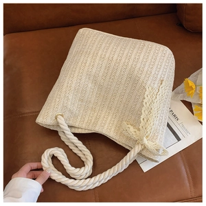 Detailed close-up of woven straw tote bag featuring lace bow and twisted cotton rope strap