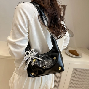 Glossy black hobo bag with pearl bow, lace trim and metal charms shown on a model